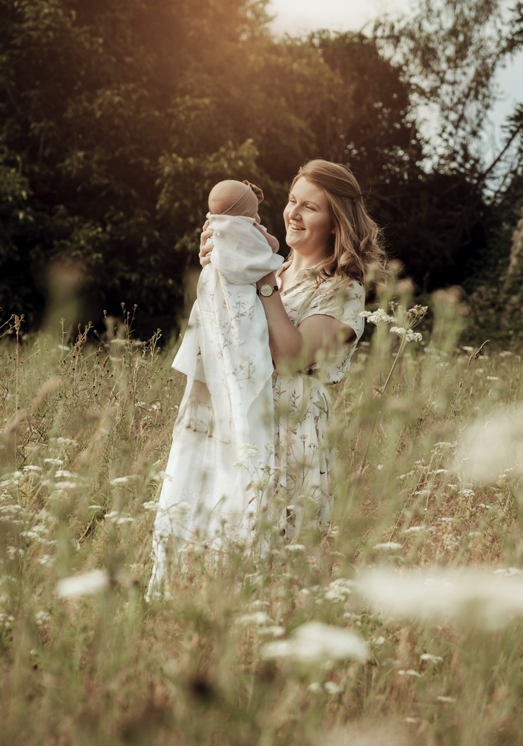 A smiling mother holding her baby wrapped in a Fenne wrap while standing in a wildflower meadow
